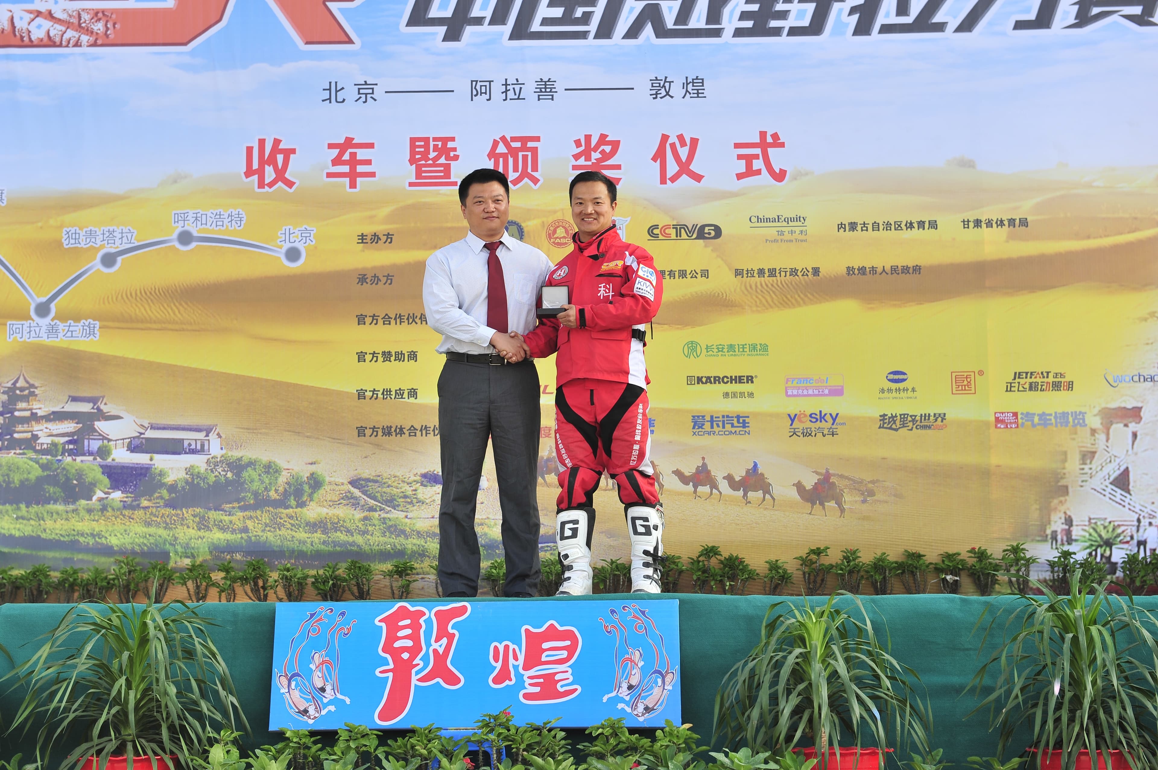 2013年李铁军身穿红色赛车服在敦煌终点领取奖项