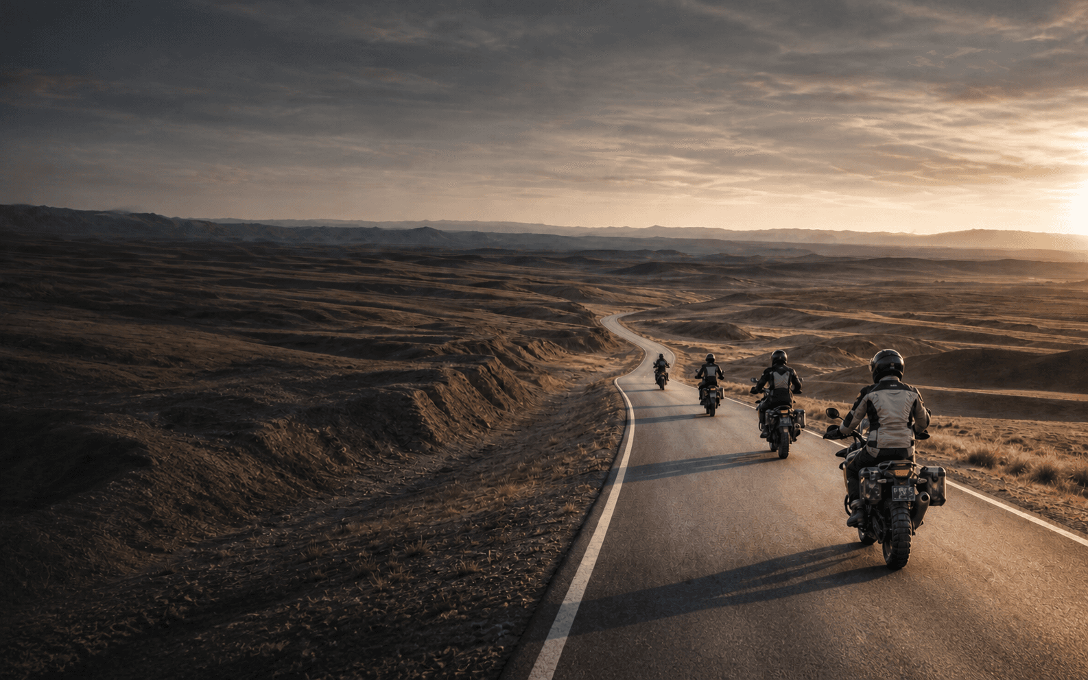 Five adventure motorcycle riders travelling west through a vast arid valley